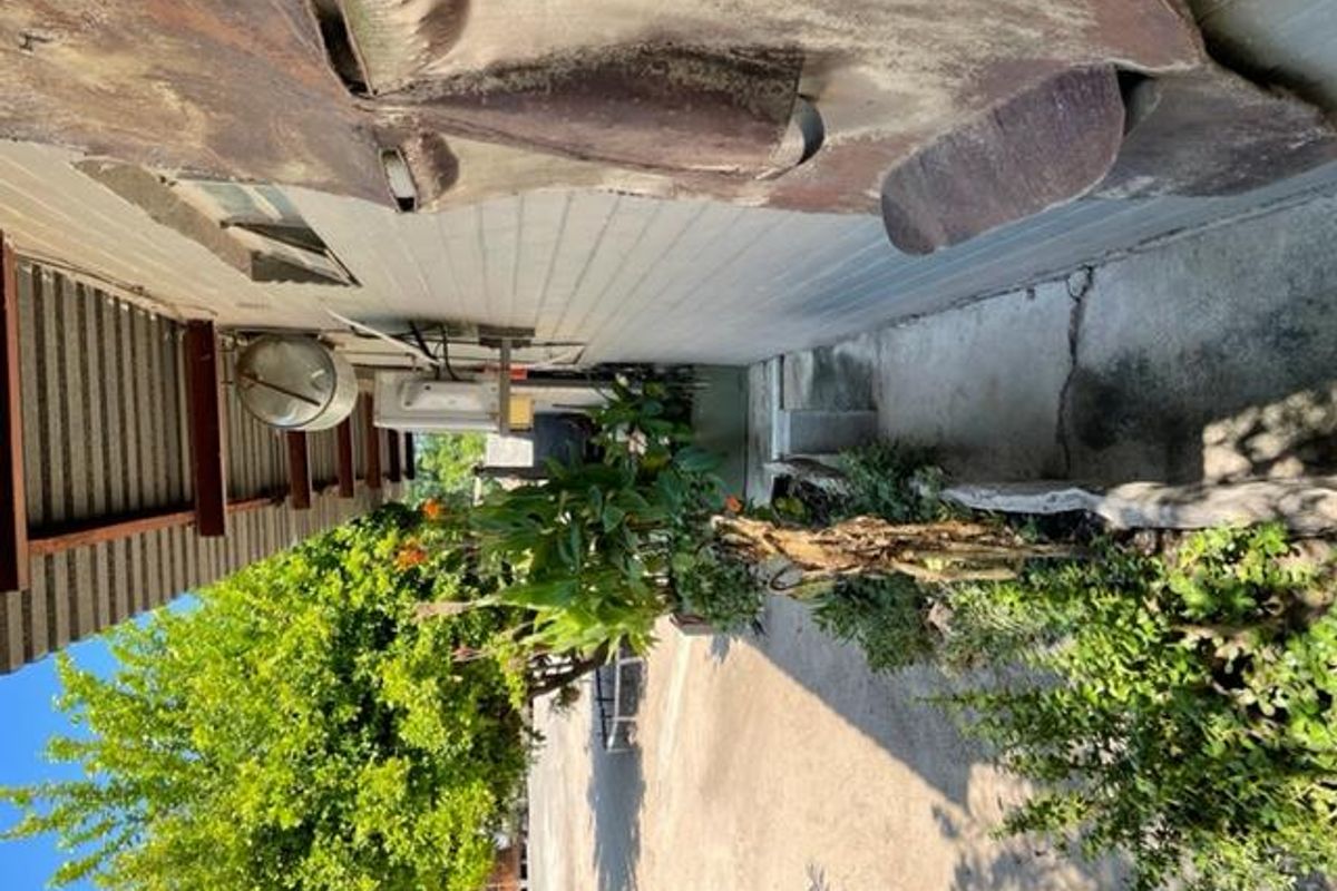 A narrow exterior side passage featuring weathered wall cladding, exposed structural beams, and concrete paving with visible cracks.