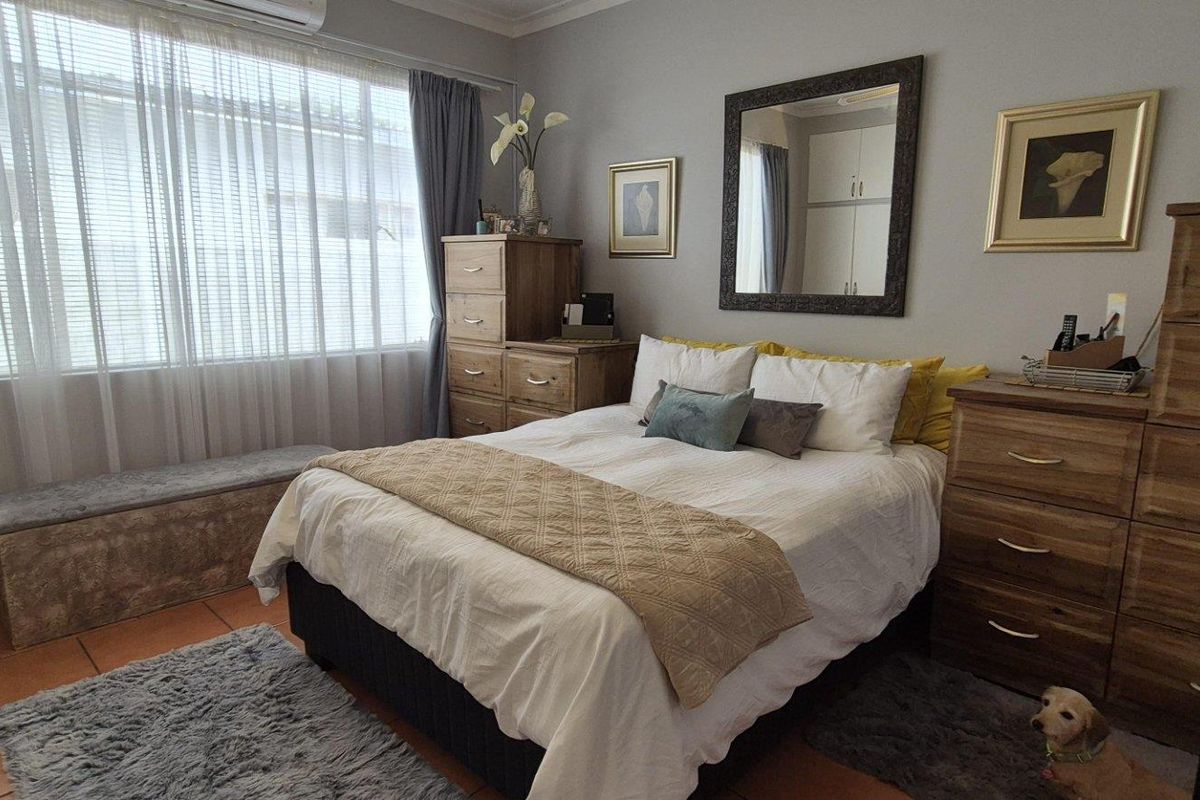 A well-maintained bedroom featuring tiled flooring, built-in cupboards, and a wall-mounted air conditioning unit.