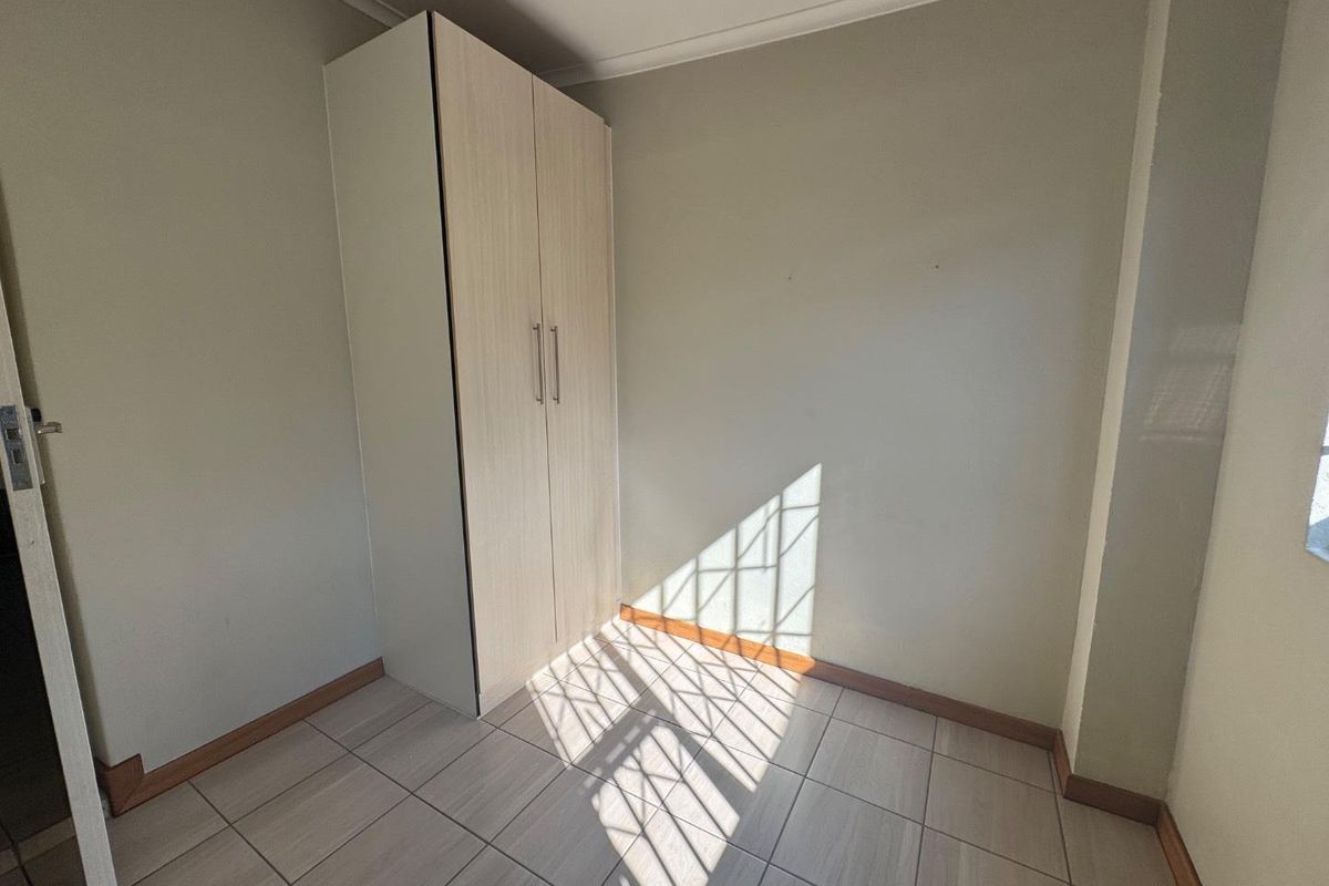 A bright, empty bedroom featuring neutral tiled flooring and a built-in wardrobe with light wood-grain finish.