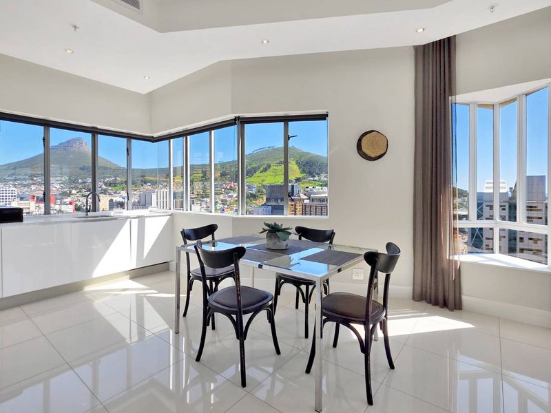 Bright open-plan living and dining area featuring high-gloss flooring, modern cabinetry, and expansive windows offering panoramic mountain and city views.