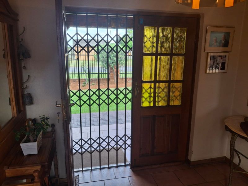 Entrance area featuring a solid timber door with decorative textured glass panels and a retractable metal security gate opening to the exterior.