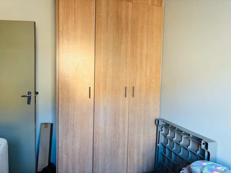 A bedroom featuring a light wood-finish built-in wardrobe with modern handles, providing ample storage space.