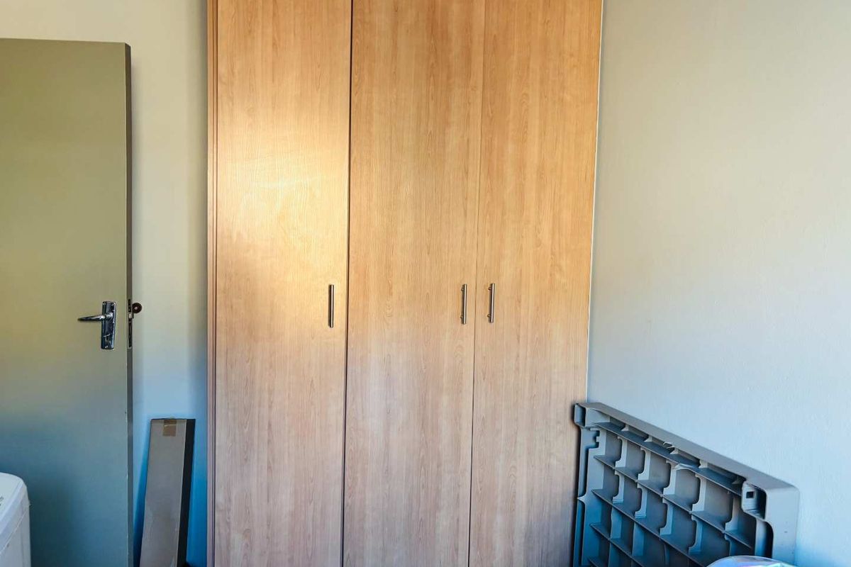 A bedroom featuring a light wood-finish built-in wardrobe with modern handles, providing ample storage space.