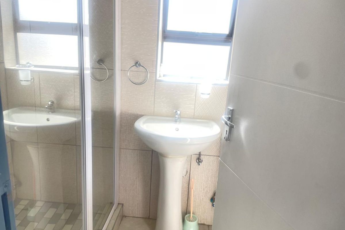 A clean, functional bathroom featuring a pedestal basin, a glass-enclosed shower, and neutral wall and floor tiling.