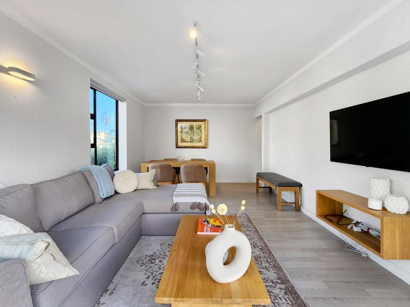 A bright and modern open-plan living and dining area featuring light laminate flooring, track lighting, and a wall-mounted television setup.