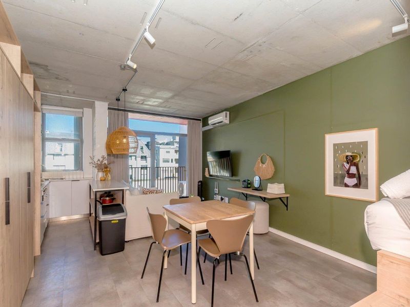 Modern open-plan studio apartment featuring an exposed concrete ceiling, kitchenette, tiled flooring, and direct access to a private balcony.
