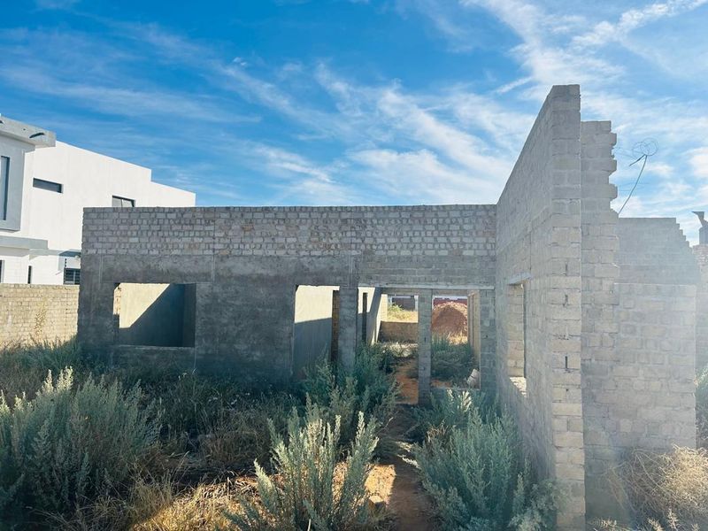 An unfinished residential structure showing exposed brick walls and concrete lintels, currently in the early stages of construction.