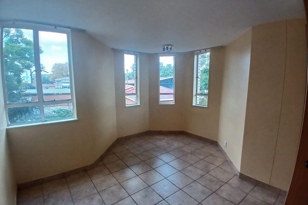 A bright, empty living area featuring tiled flooring and multiple windows providing natural light and neighborhood views.