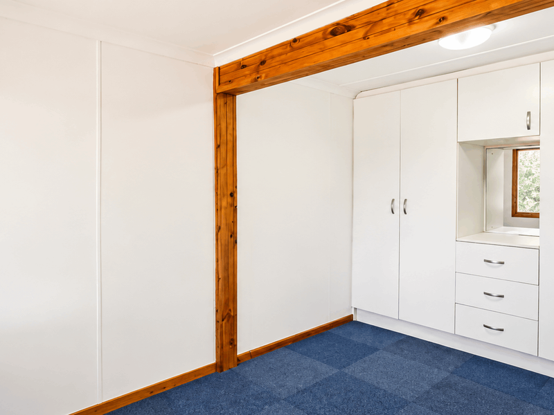 A clean, empty bedroom featuring built-in white cabinetry, a central timber ceiling beam, and blue carpet flooring.