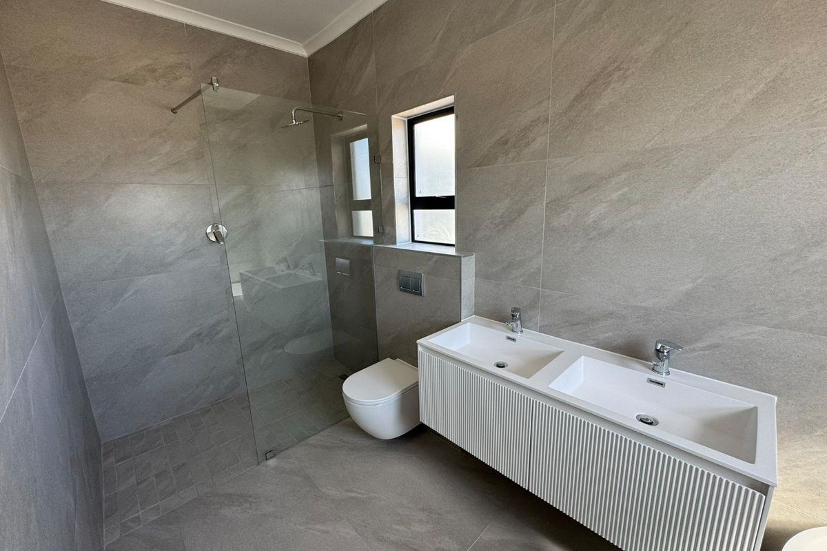 Modern bathroom featuring a frameless glass walk-in shower, wall-mounted toilet, and a contemporary double vanity with integrated sinks and textured cabinetry.