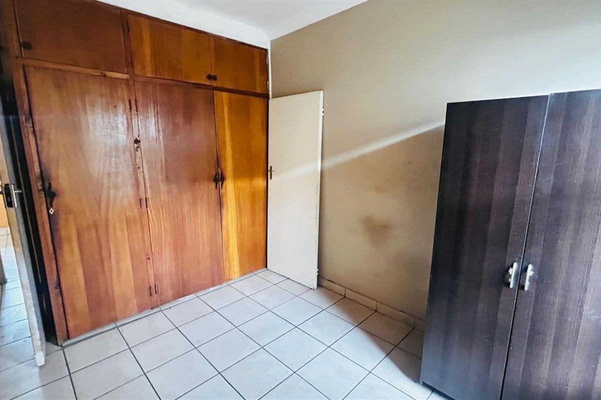 A bedroom featuring tiled flooring and built-in wooden cupboards, offering a functional space with potential for cosmetic updates.