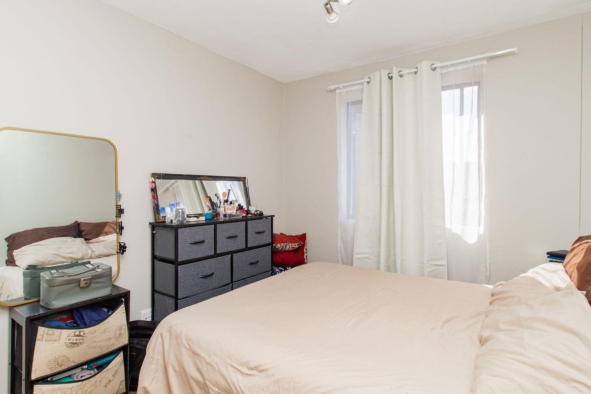 A functional bedroom featuring neutral wall tones, a window with curtain tracks, and overhead lighting.