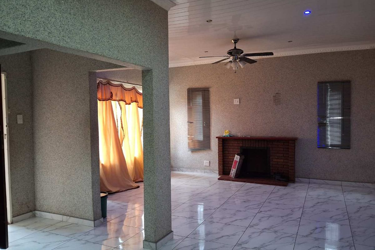 Spacious living area featuring marble-look tiled flooring, a brick fireplace, and a ceiling fan, offering a versatile layout for comfortable family living.