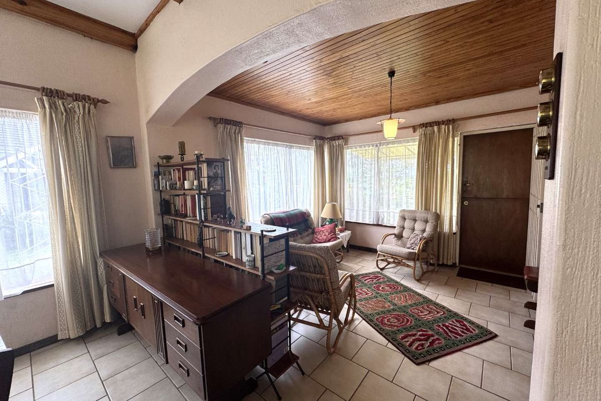 A living area featuring a timber-paneled ceiling, tiled flooring, and an arched architectural transition, providing a cozy and traditional atmosphere.