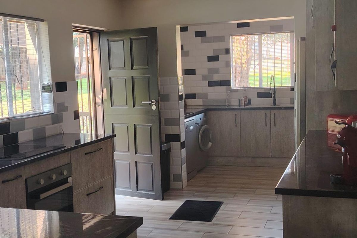 Modern kitchen featuring granite countertops, built-in oven, hob, and a separate scullery area with tiled finishes and direct outdoor access.