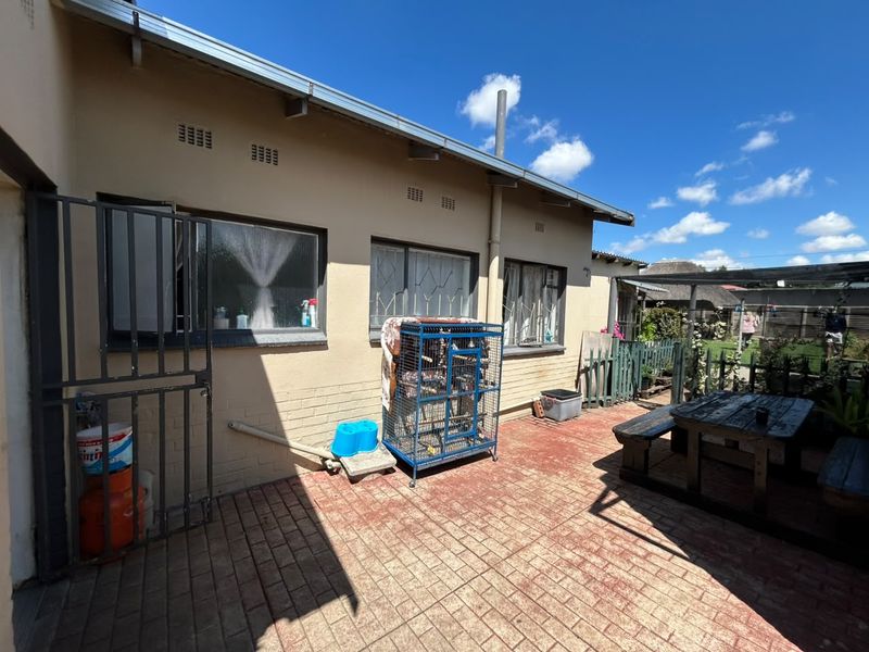 Rear exterior view of the property featuring a paved patio area, security gates, and brick facade with security bars on the windows.