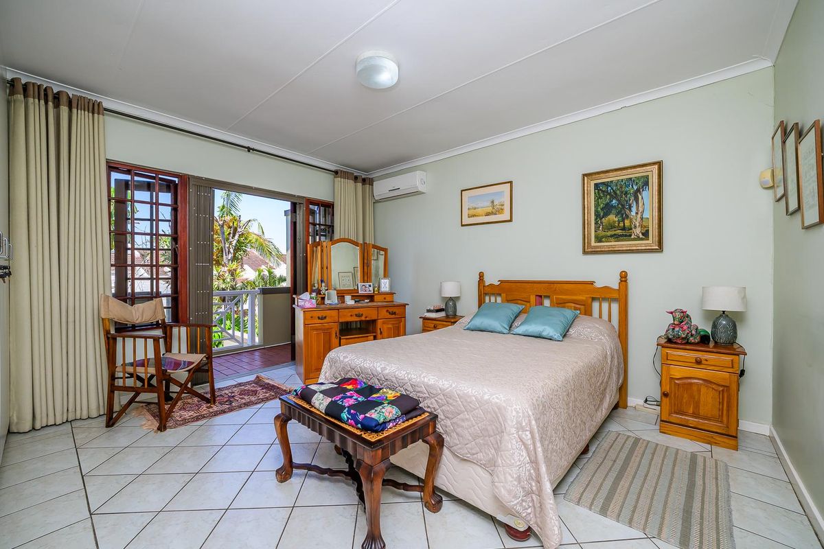 A well-lit bedroom featuring tiled flooring, a wall-mounted air conditioning unit, and direct access to a private balcony through wooden framed doors.