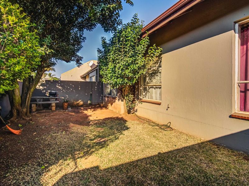 A rear garden area featuring a boundary wall, established trees, and a mix of lawn and exposed soil, providing a private outdoor space.