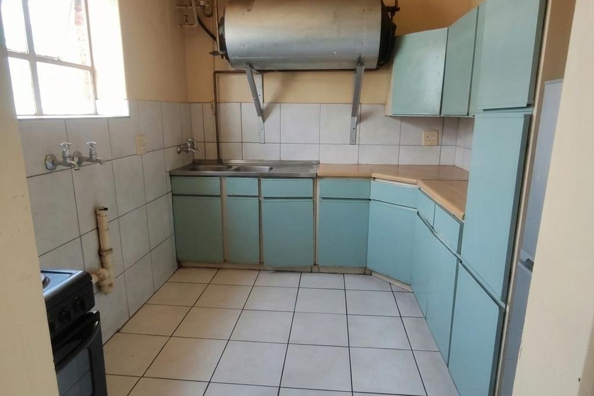 A functional kitchen featuring dated cabinetry, tiled splashbacks, and exposed plumbing. The space offers a practical layout with potential for modern renovation.