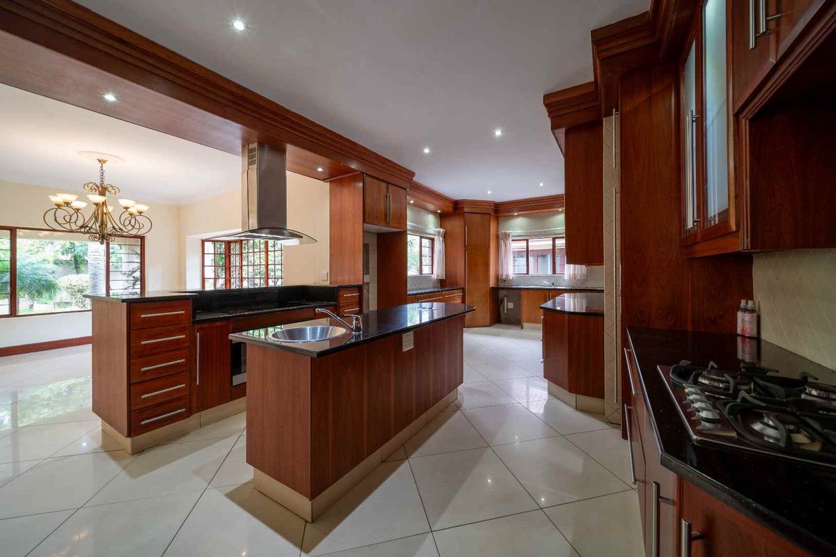 Spacious kitchen featuring dark wood cabinetry, granite countertops, a central island with a prep sink, and a gas hob, offering ample storage and workspace.
