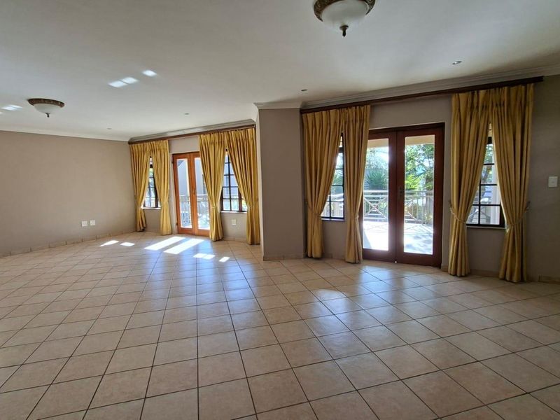 Spacious, open-plan living area featuring neutral tiled flooring, abundant natural light through double glass doors, and an elegant wrought iron staircase.