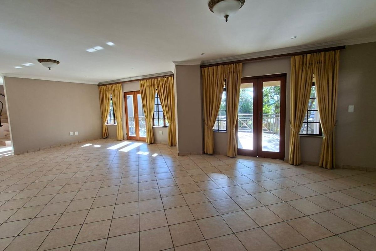 Spacious, open-plan living area featuring neutral tiled flooring, abundant natural light through double glass doors, and an elegant wrought iron staircase.