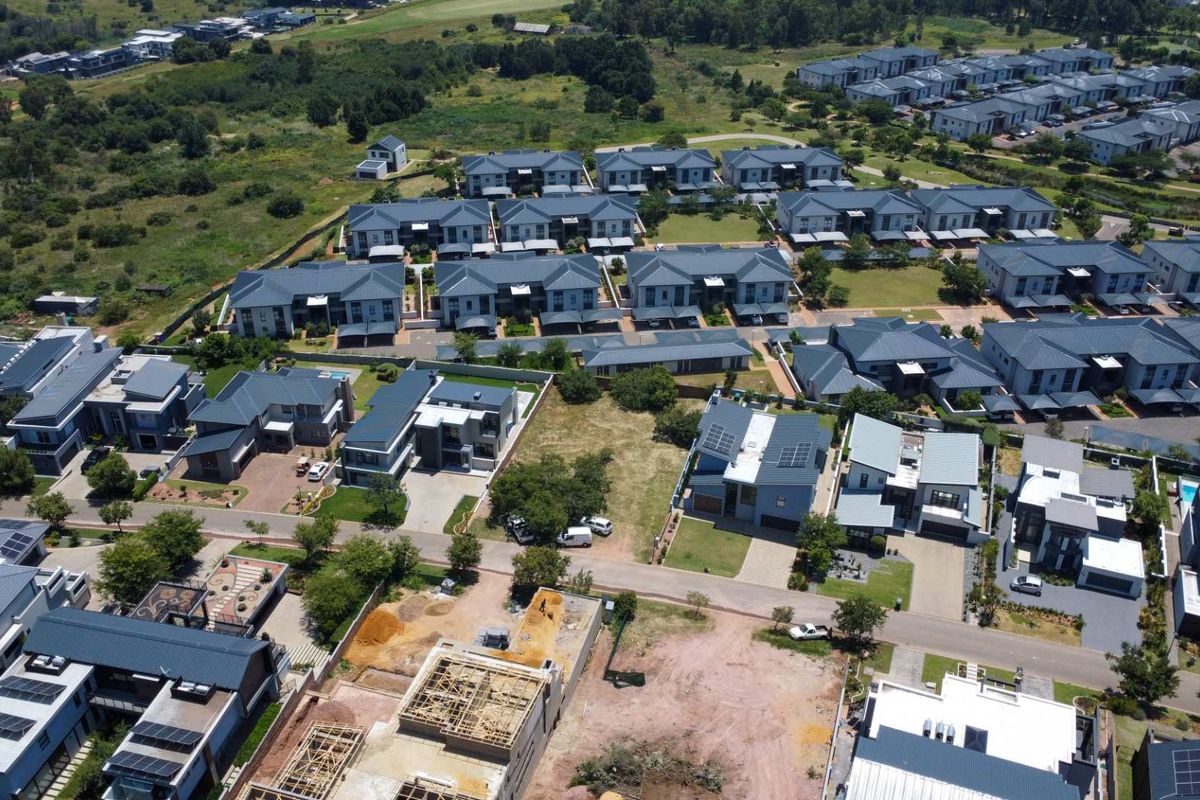 Aerial view of a residential estate featuring modern homes, paved roads, and a vacant plot currently under construction.