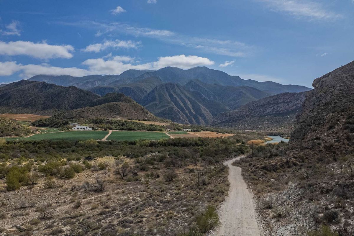 An aerial view of the farm property featuring a dirt access road, expansive agricultural fields, a river, and a scenic mountain backdrop.