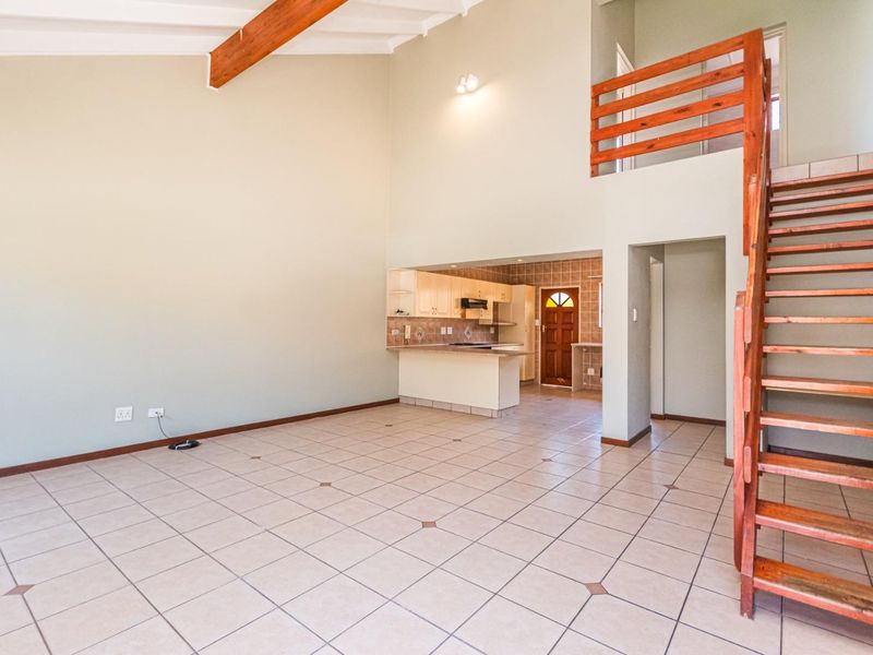 Spacious open-plan living area featuring vaulted ceilings with exposed timber beams, ceramic tiled flooring, and a wooden staircase leading to an upper level.