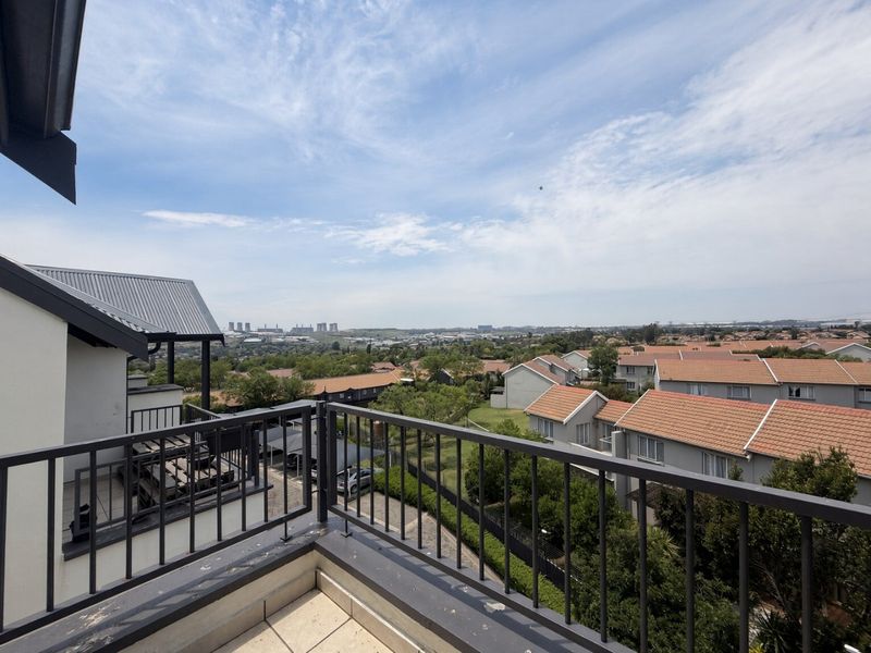 A spacious balcony featuring a metal balustrade and tiled flooring, offering expansive elevated views over the surrounding residential estate.