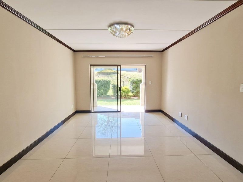 Spacious, empty living room featuring polished porcelain floor tiles, crown molding, and a sliding glass door leading to an outdoor area.