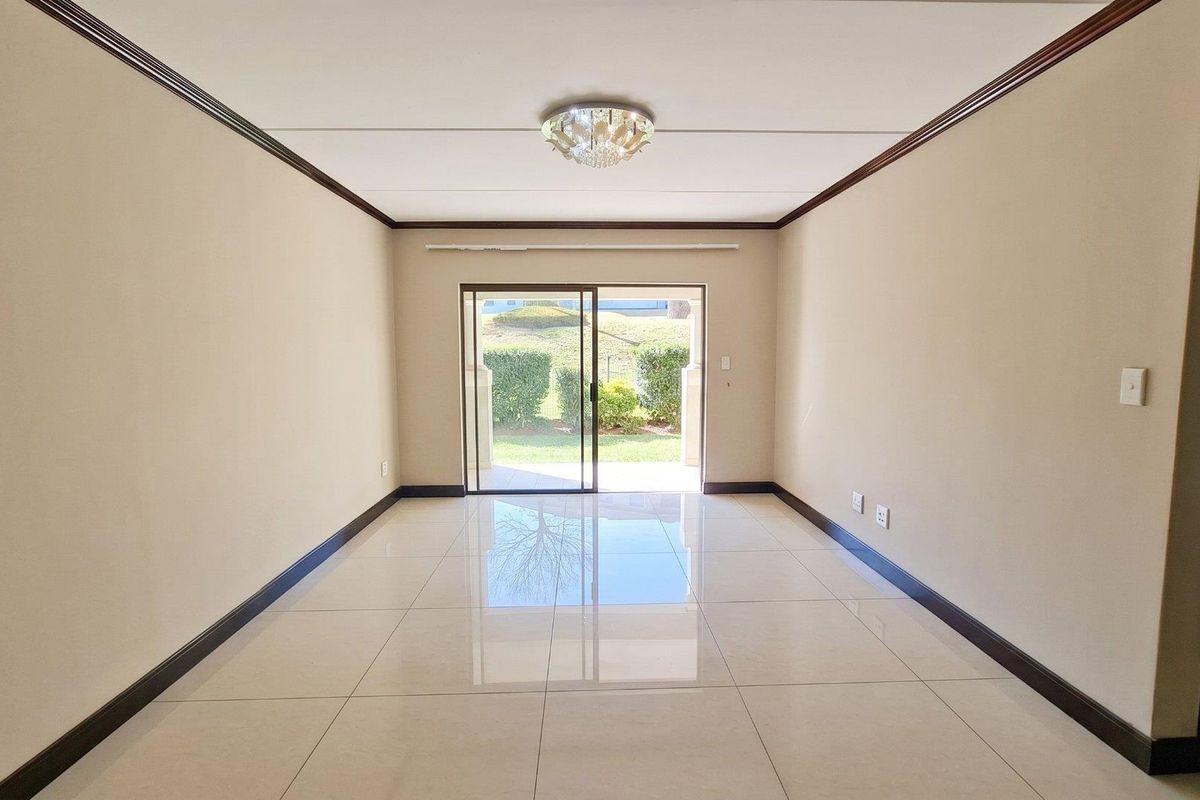 Spacious, empty living room featuring polished porcelain floor tiles, crown molding, and a sliding glass door leading to an outdoor area.