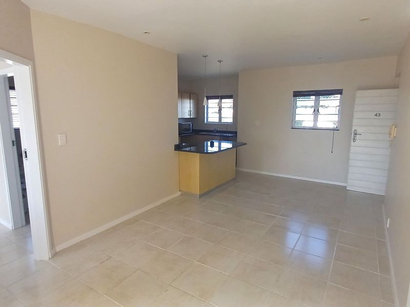 An open-plan living and kitchen area featuring tiled flooring, a kitchen island with granite countertops, and neutral wall finishes.