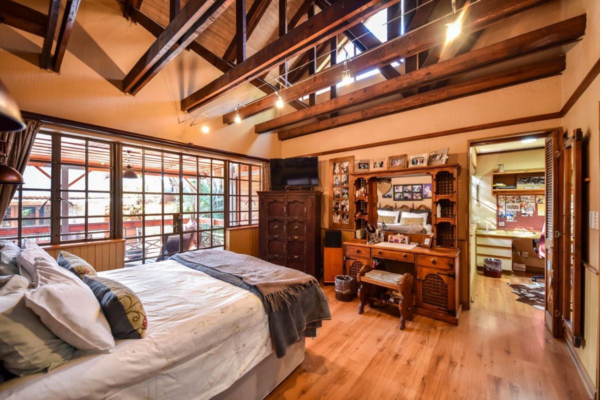 Spacious bedroom featuring high vaulted ceilings with exposed timber beams, timber flooring, and large glass sliding doors opening to an outdoor area.