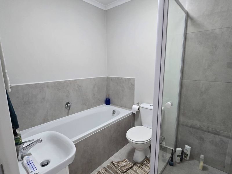 Modern bathroom featuring a built-in bathtub, separate shower enclosure, pedestal washbasin, and toilet with neutral grey wall tiling.