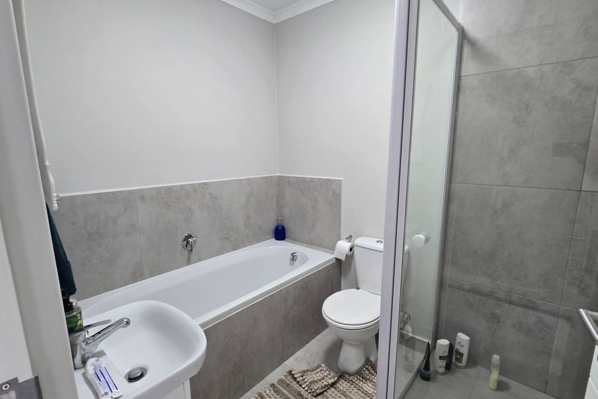 Modern bathroom featuring a built-in bathtub, separate shower enclosure, pedestal washbasin, and toilet with neutral grey wall tiling.