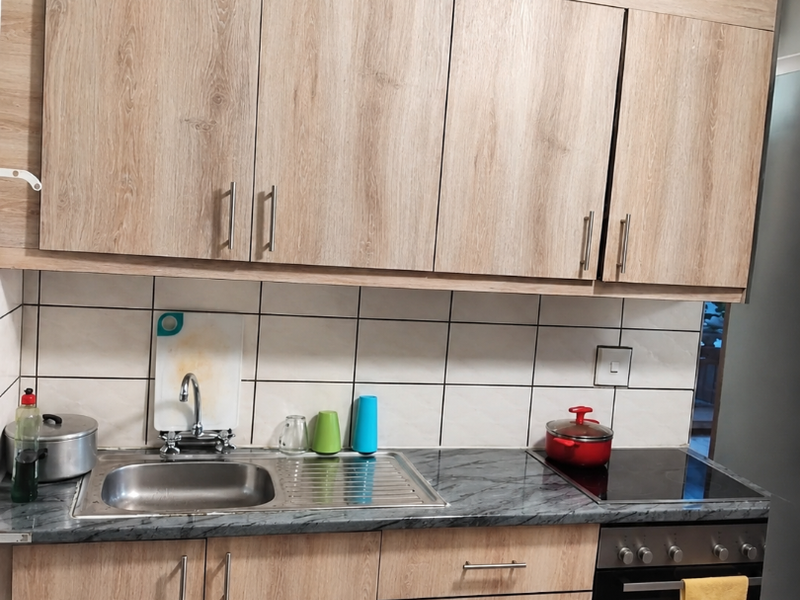 A functional kitchen featuring light wood-grain cabinetry, marble-effect countertops, a stainless steel sink, and integrated oven with electric cooktop.