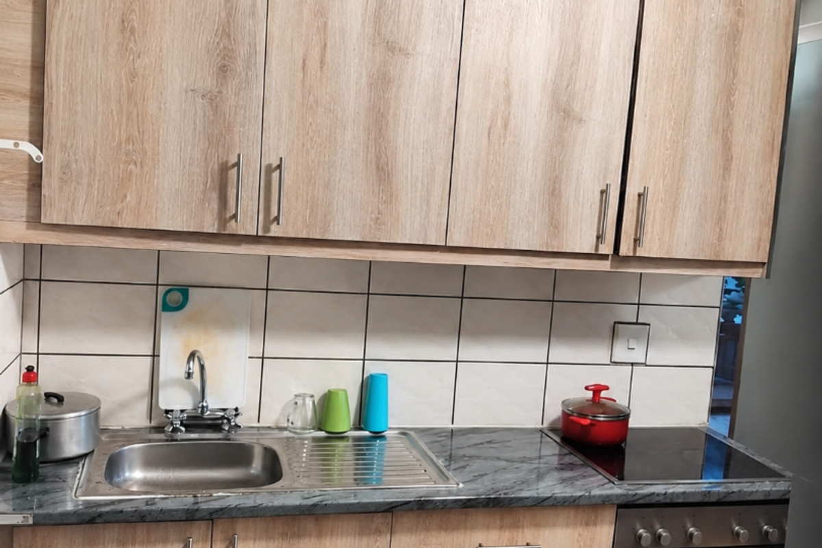 A functional kitchen featuring light wood-grain cabinetry, marble-effect countertops, a stainless steel sink, and integrated oven with electric cooktop.