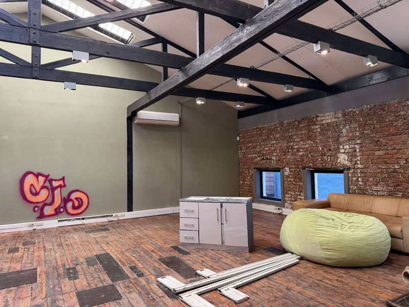 Spacious open-plan office area featuring exposed timber roof trusses, brick feature walls, skylights, and hardwood flooring, offering a unique industrial aesthetic.