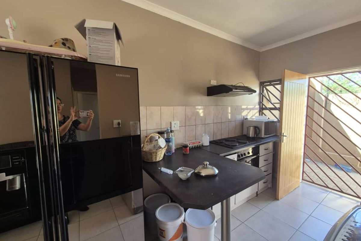 A functional kitchen featuring a built-in oven, electric hob, extractor fan, tiled backsplash, and direct access to an outdoor area via a security gate.