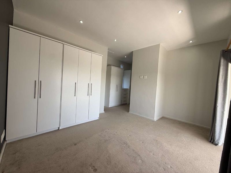 A spacious, neutral bedroom featuring extensive built-in cupboard storage, recessed downlighting, and carpeted flooring.