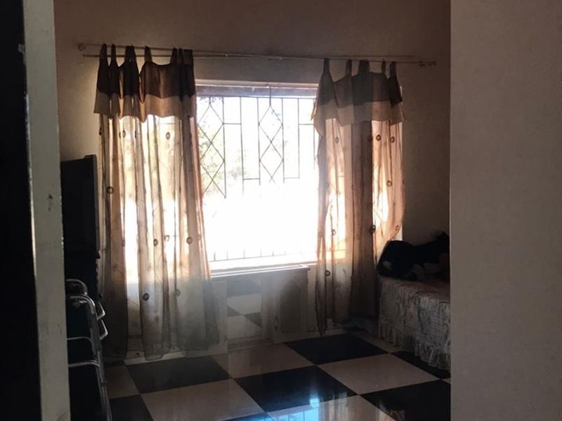 A bedroom featuring a distinctive checkered tile floor and an exposed timber beam ceiling, equipped with security burglar bars on the window.