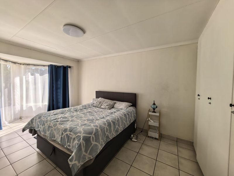 A bedroom featuring tiled flooring, built-in cupboards, and a large window allowing natural light.