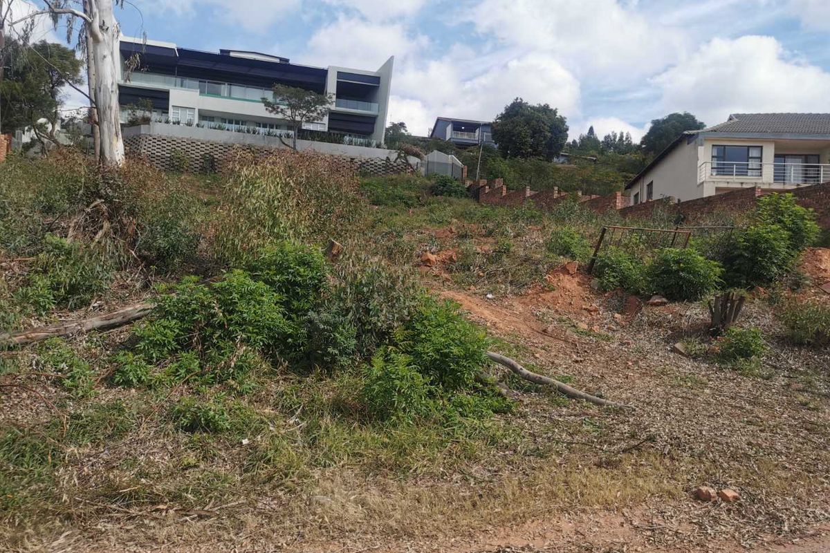 A sloped vacant residential plot featuring natural vegetation and surrounding established residential properties in an elevated neighborhood setting.