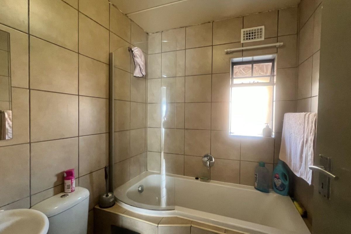 A functional bathroom featuring a built-in bathtub with a glass shower screen, wall-mounted faucet, and full-height ceramic wall tiling.