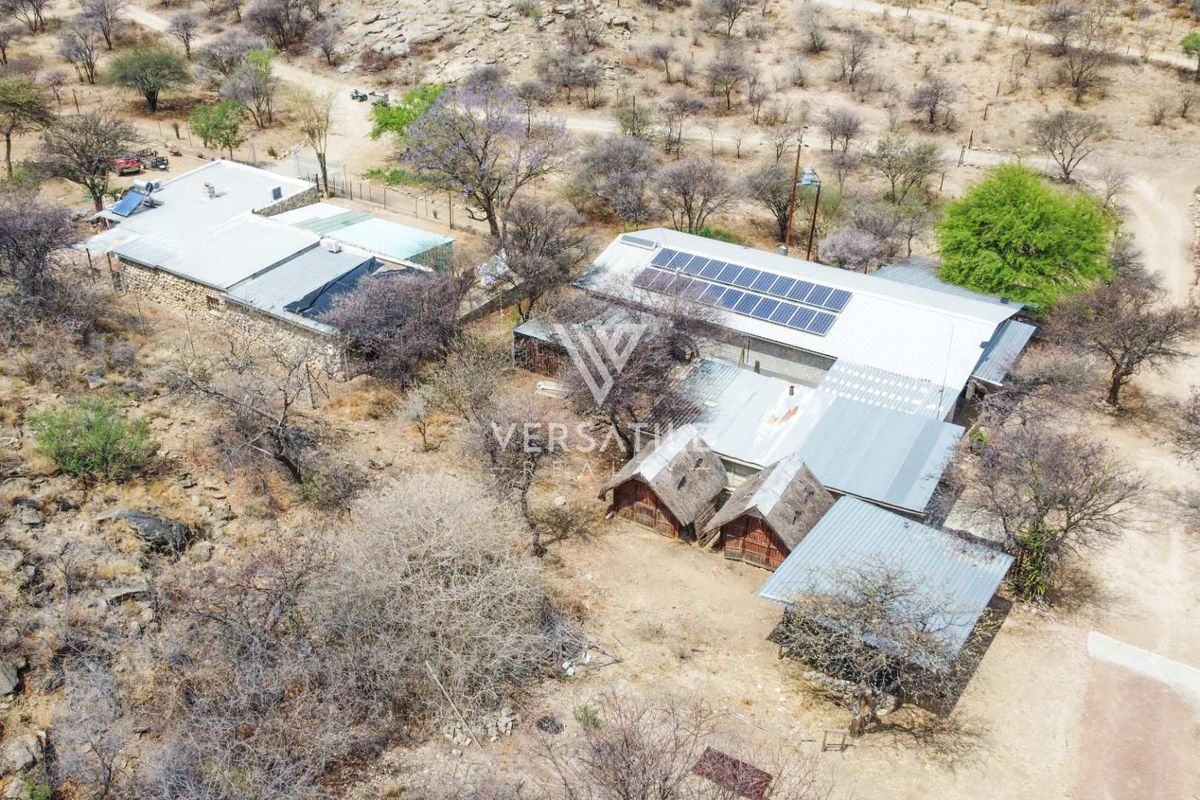 Aerial view of the small holding property featuring multiple structures with metal and thatch roofing, equipped with solar panels and a solar geyser system.