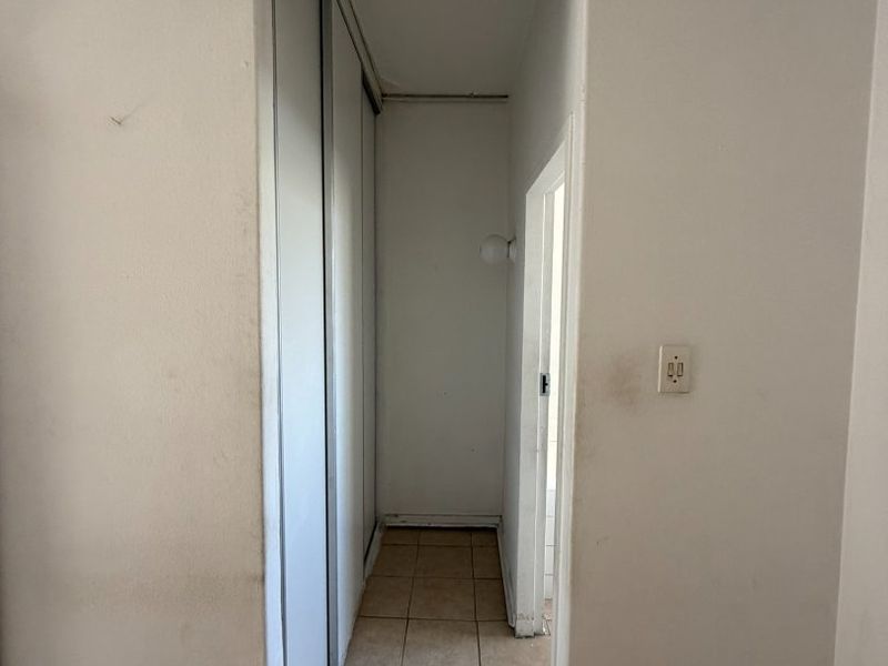 A narrow hallway featuring built-in sliding door cupboards and tiled flooring, requiring cosmetic updates to the wall finishes and fixtures.