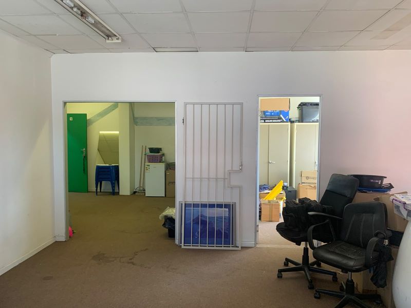 An office space featuring a suspended ceiling, carpeted flooring, and two doorways, one secured with a metal gate.