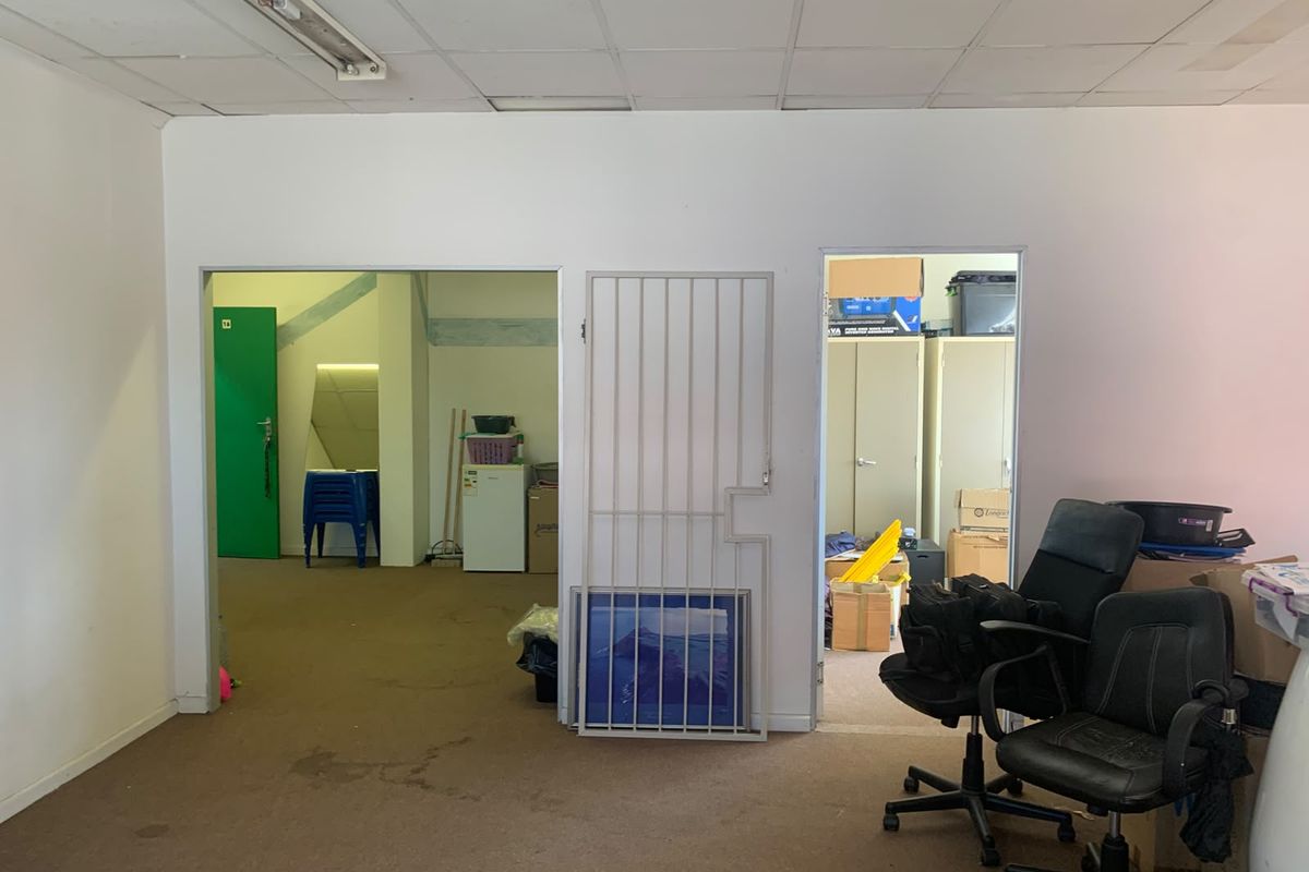 An office space featuring a suspended ceiling, carpeted flooring, and two doorways, one secured with a metal gate.
