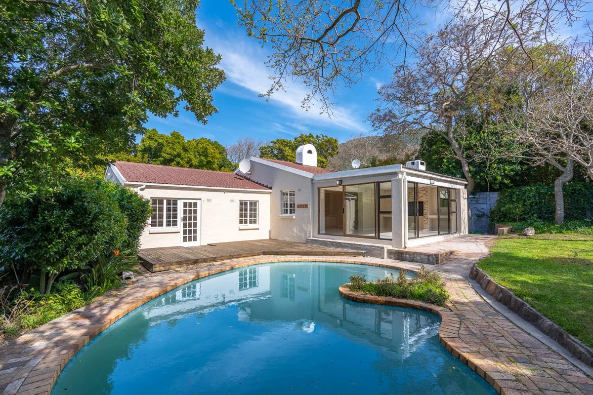 Rear view of the house featuring a swimming pool, wooden decking, and large sliding glass doors leading into the living area.